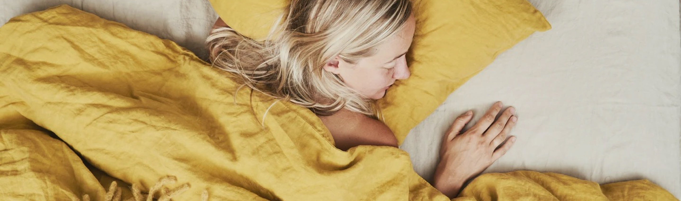 A blonde model sleeps on mustard colored linen bedding by Hawkins New York
