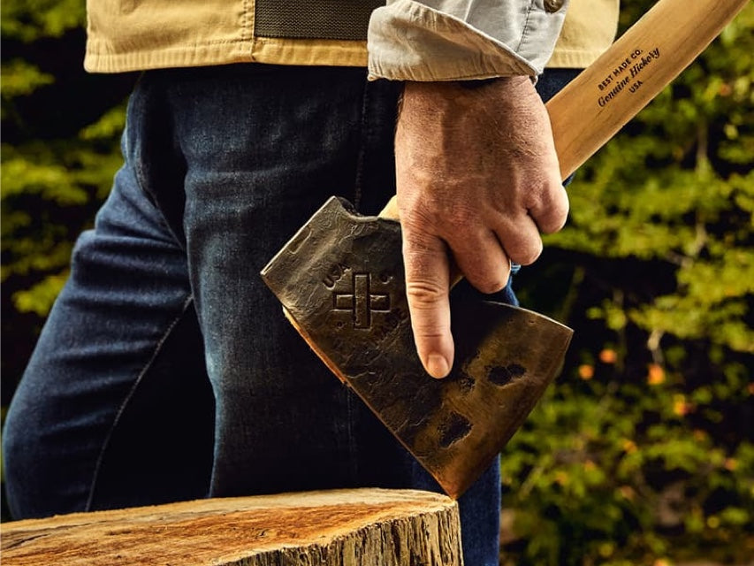 A man holds a Best Made axe in an outdoor setting with a wood chopping block.