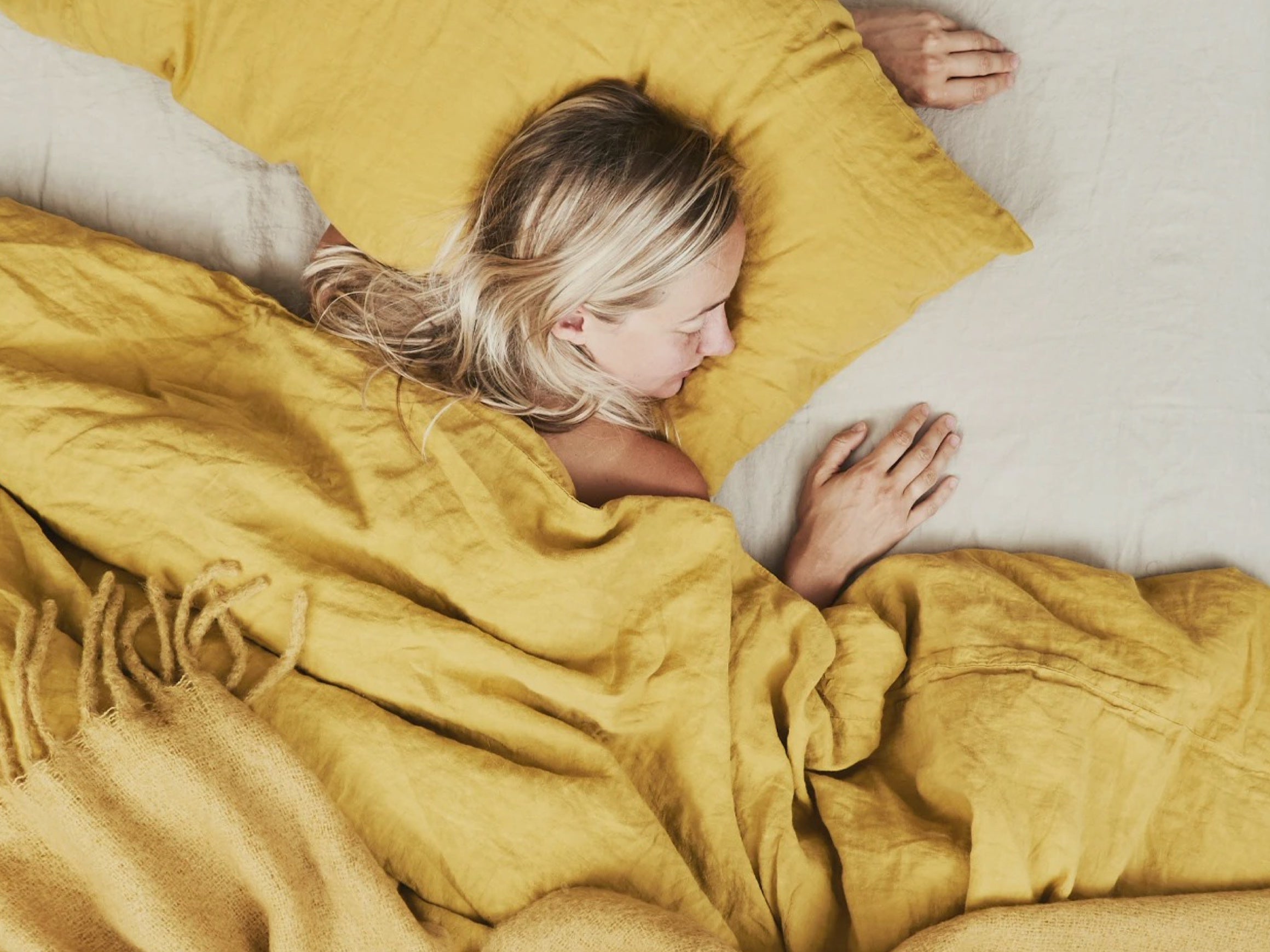 A woman sleeps on mustard and flax linens by Hawkins New York.